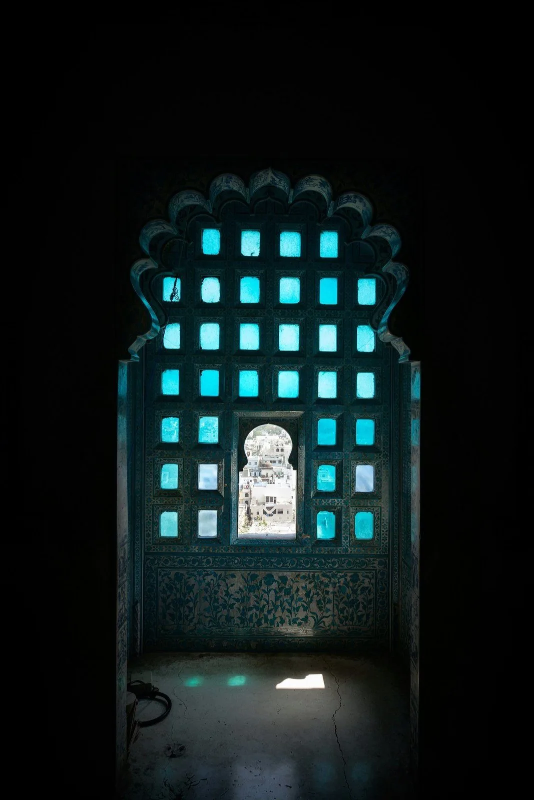 Glowing stained-glass jharokha window in a darkened palace room