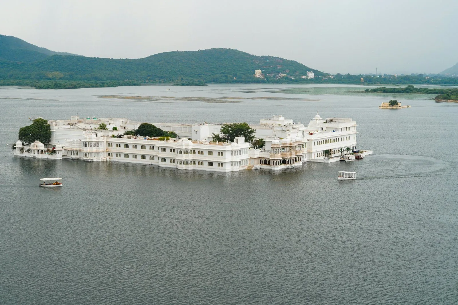 A white lake palace resting alone on still water, hills beyond